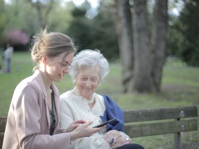 Young woman sitting with old woman in bench on a park