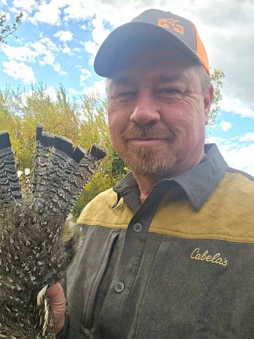 Man holding a bird with a smile outdoors.