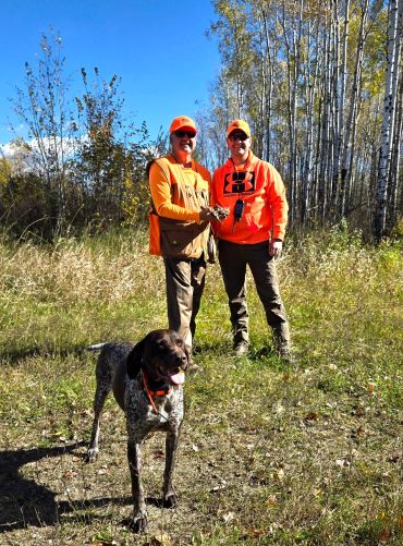 Two hunters with a dog in the woods.