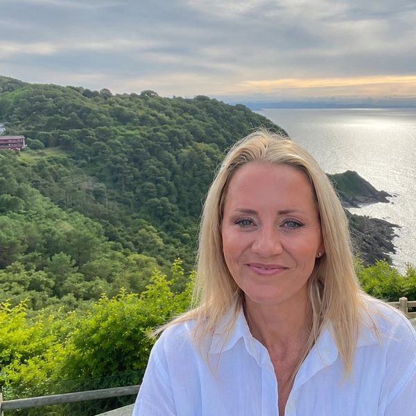 Smiling woman with scenic ocean and green hills in background.