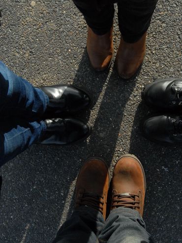 Four people wearing different shoes standing in a circle on asphalt.