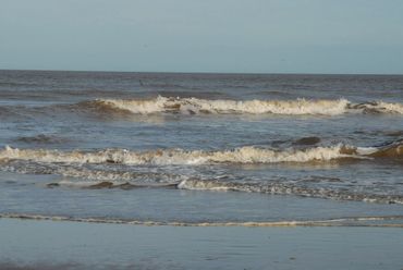 Gentle waves rolling onto a sandy beach under a clear sky.