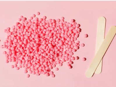 Pink wax beads and wooden spatulas on a pink background for hair removal.