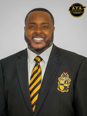 Man in a black blazer with a crest and striped tie.