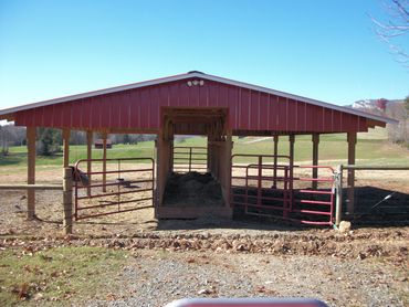Red farm shelter with metal gates in a rural field under clear blue sky.