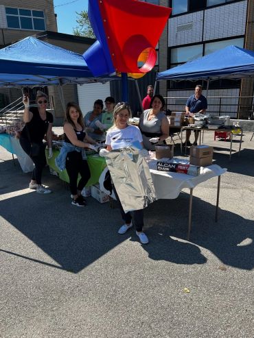 Group of people at outdoor event with food tables under blue tents.