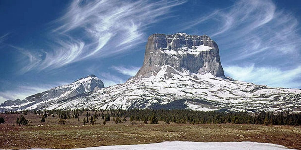 Snow-capped mountain with a flat summit under wispy clouds and a clear blue sky.