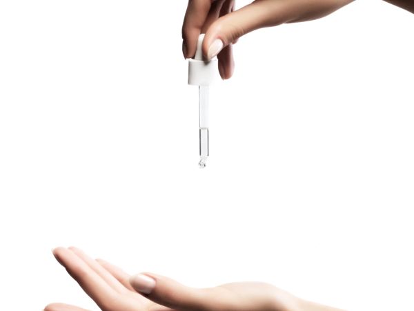 Hand applying serum with dropper over open palm against white background.
