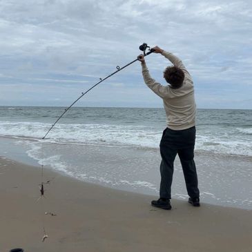 Person casting a fishing line on a cloudy beach shore.