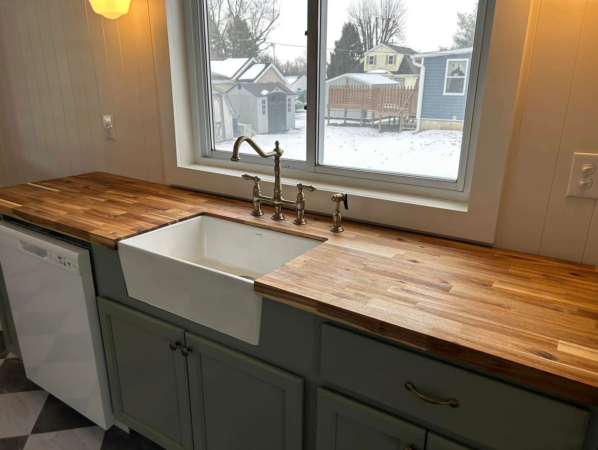 Kitchen sink with wooden countertop and snowy backyard view.
