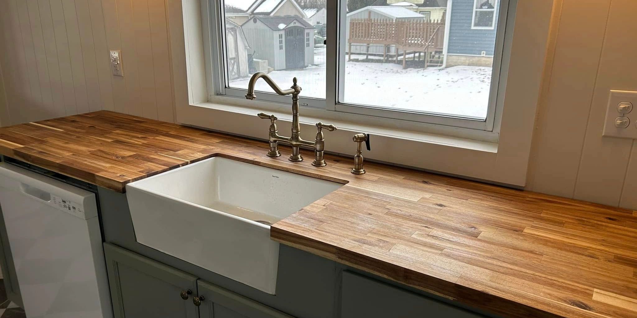 Kitchen sink with wooden countertop and snowy backyard view.