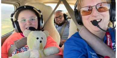 Family flying together in a small plane, smiling and holding a teddy bear.