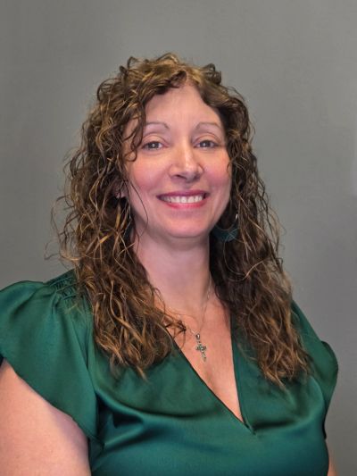 Woman with curly hair smiling in a green blouse.