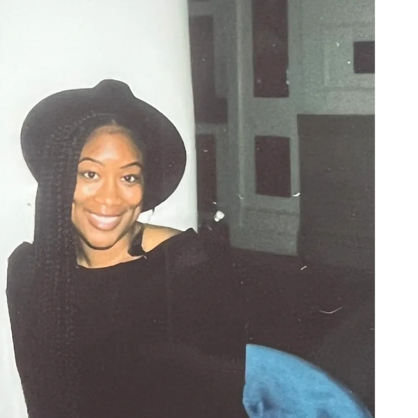 Smiling woman with long braids wearing a black hat and top.