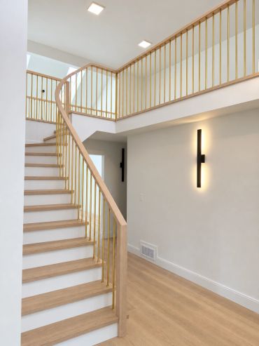 Modern wooden staircase with gold railing and minimalistic wall light.