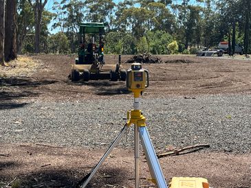 Surveying equipment set up at a construction site with a grader in the background.