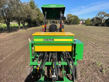 Green and yellow mini-seeder attached to a tractor in a field.