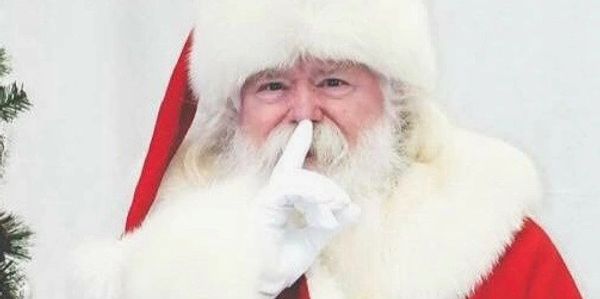 Santa Claus making a shushing gesture with his finger to his lips.