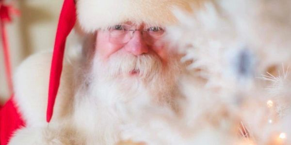 Close-up of Santa Claus with glasses and red hat, smiling warmly.
