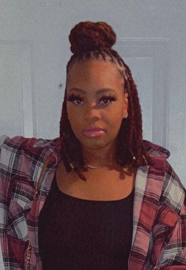 Woman with braided hair styled in a bun, wearing a plaid shirt over a black top.