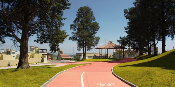 A red bike path winding through a park with trees and a gazebo.