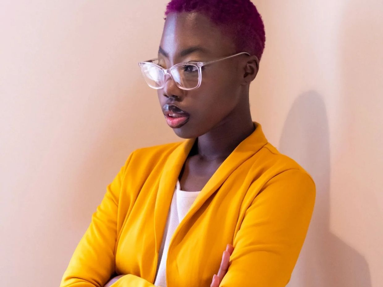 Somidinla in a yellow suit, clear glasses, and short purple shaved hair.