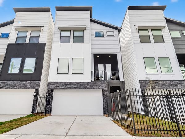 Modern three-story townhouses with garages and fenced yards under a blue sky.