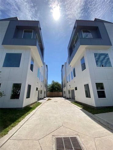 Modern white and gray townhouses under a bright sun and blue sky.