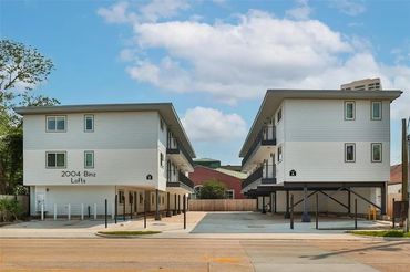 Modern white apartment buildings with parking underneath and clear blue sky.