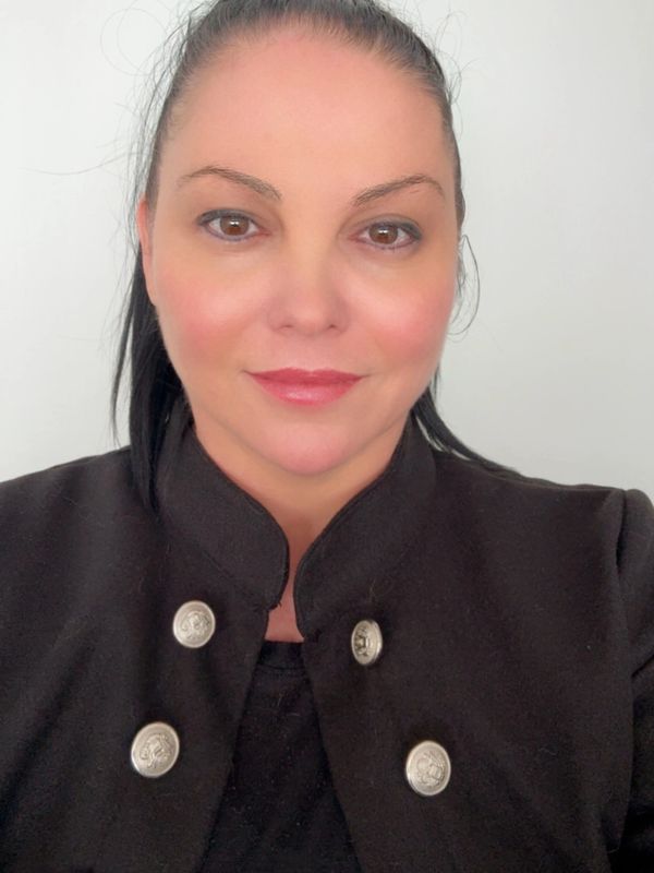 Woman with dark hair in a black jacket with silver buttons, smiling gently.