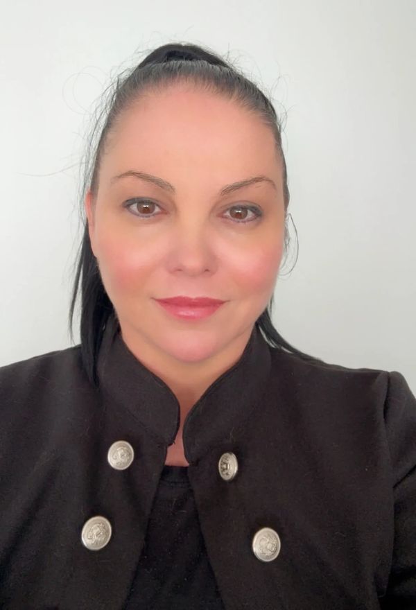 Woman with dark hair in a black jacket with silver buttons, smiling gently.