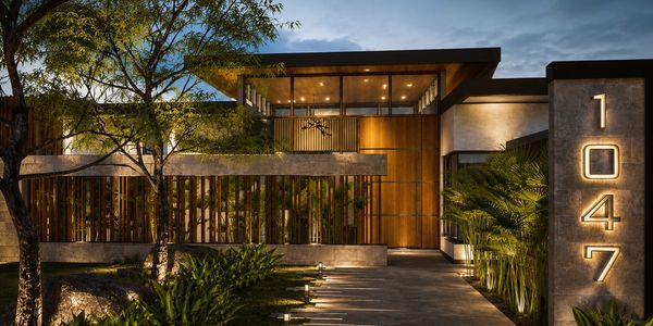 Modern house exterior with warm lighting and natural landscaping at dusk.