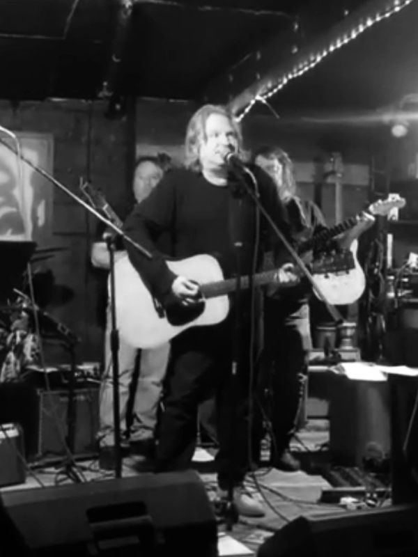 Band performing on stage with guitars and microphones in a dimly lit venue.