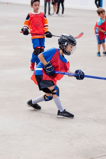 Young boys playing street hockey wearing protective gear and red jerseys.