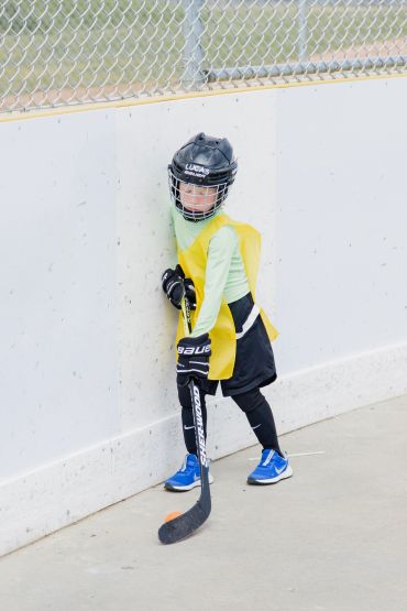 Young child in hockey gear standing by rink wall with stick.