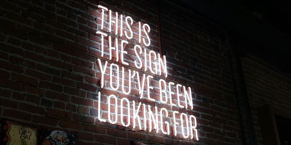 Neon sign on brick wall with motivational message.