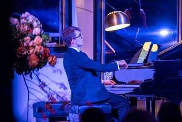 A young man in a suit plays piano under soft lighting.