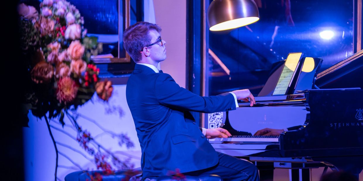 A man in a suit passionately playing a grand piano under soft lighting.