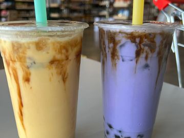 Two colorful iced bubble tea drinks with straws on a table.