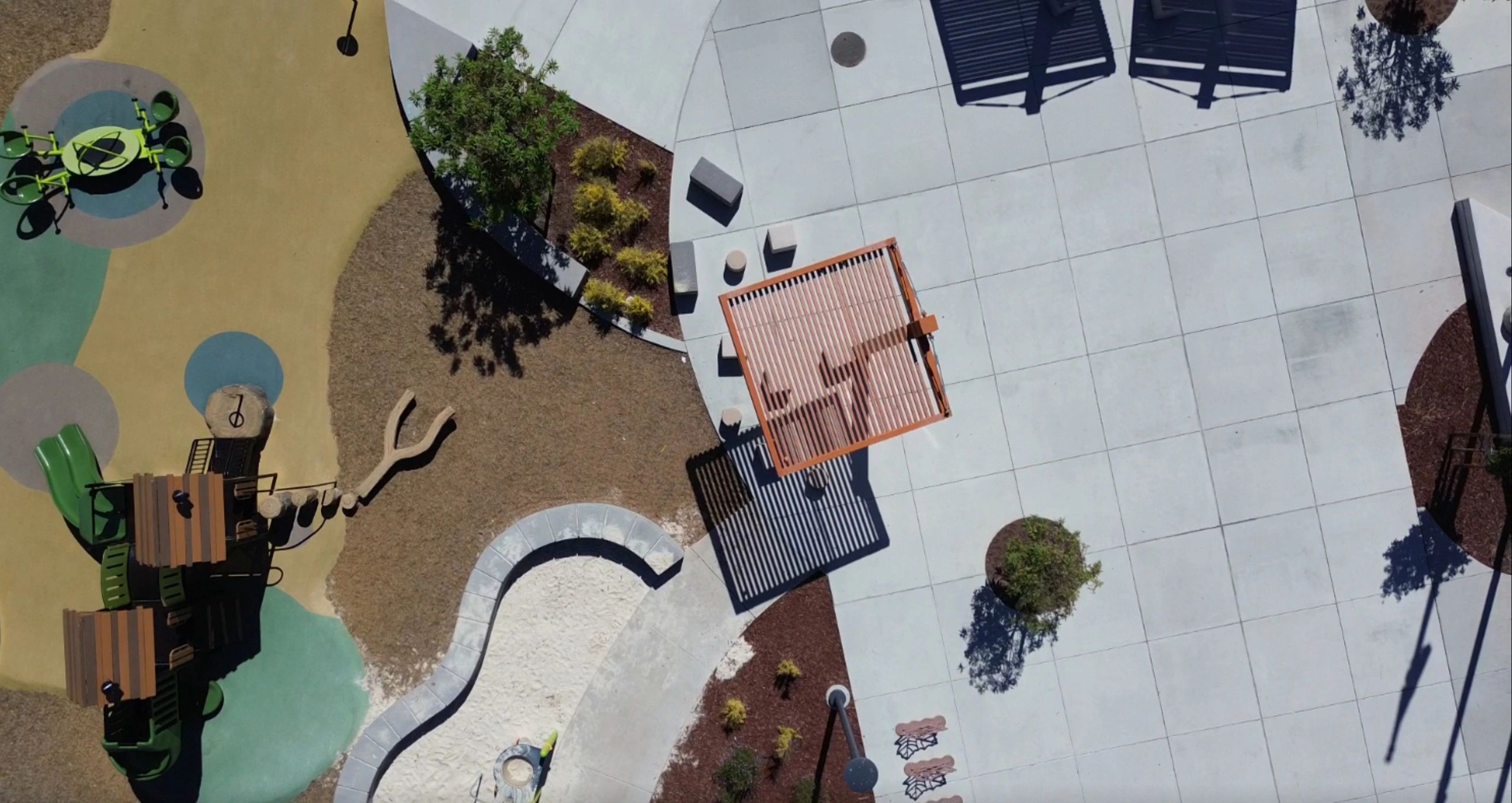 Aerial view of a playground with slides, sandpit, and shaded seating area.