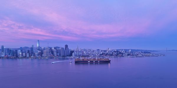 Cargo ship sailing near a city skyline during twilight hours.