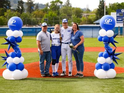 Family stands on baseball field with balloons.