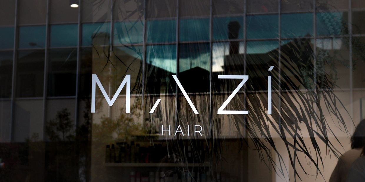 Window sign for Mazi Hair salon with reflections of surroundings.