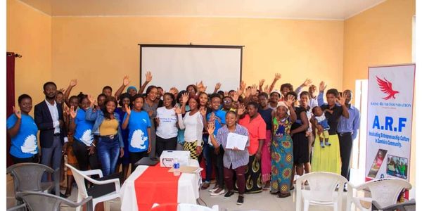 Group photo of diverse people smiling and waving indoors.