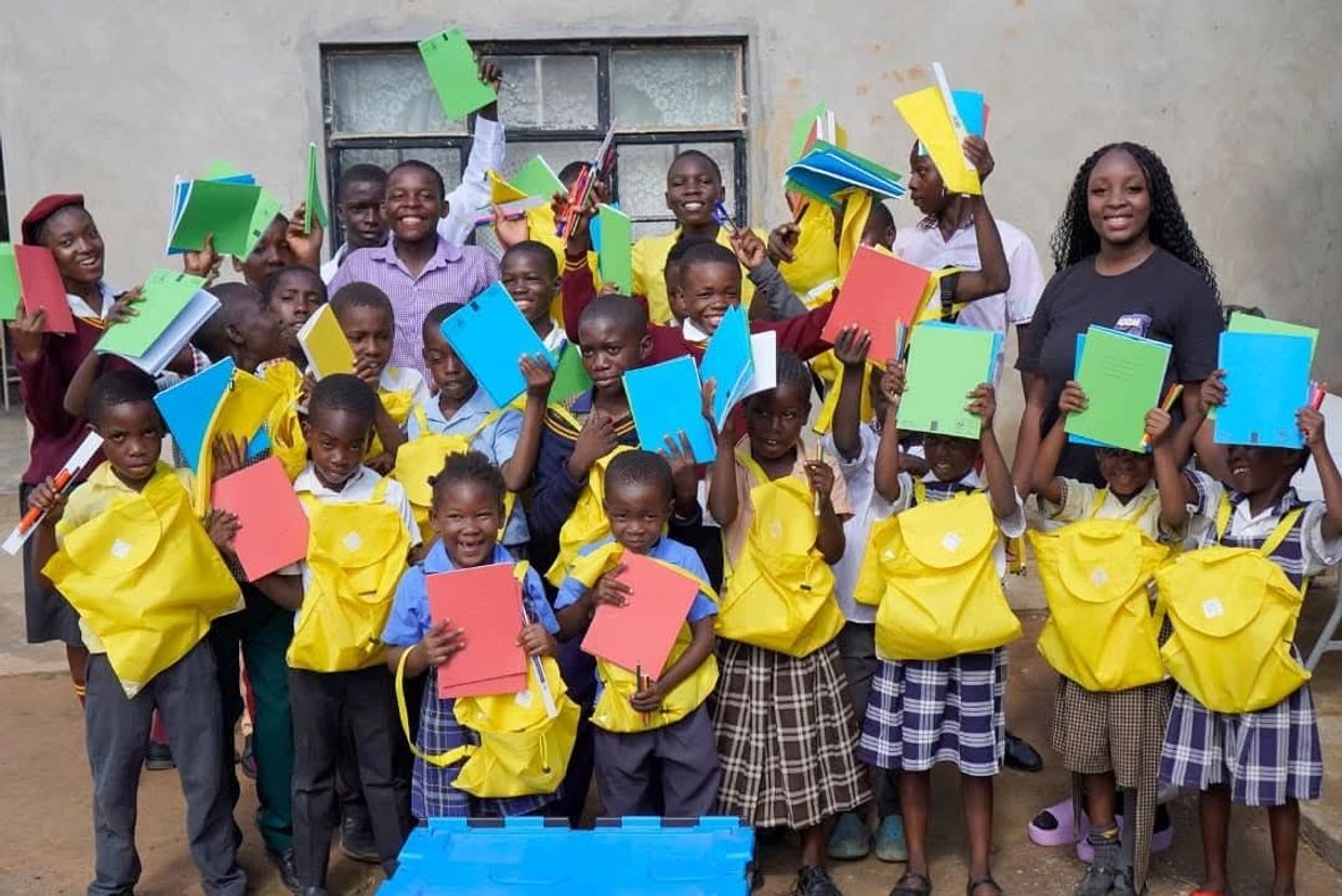 Group of smiling children holding colorful notebooks and yellow backpacks.