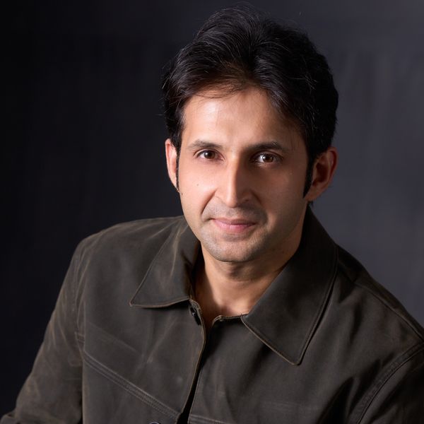 Man wearing a brown jacket with a gentle smile.