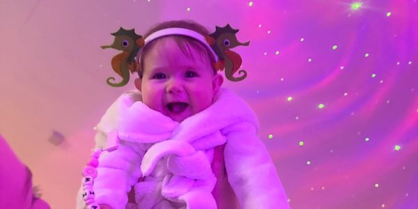 Smiling baby in cozy outfit with seahorse headband under starry purple light.