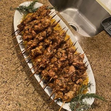 Skewers of seasoned grilled meat arranged on a white platter.
