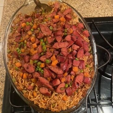 Casserole dish with rice, sliced sausage, peas, and carrots.