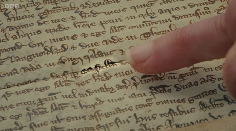 Finger pointing at ancient manuscript text.